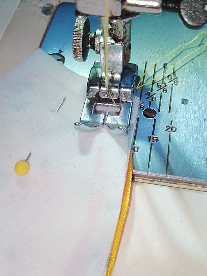 Sewing around the curved edge of an ear piece on a sewing machine using a 6 mm (¼ inch) seam allowance, stitching smoothly while leaving the base open.