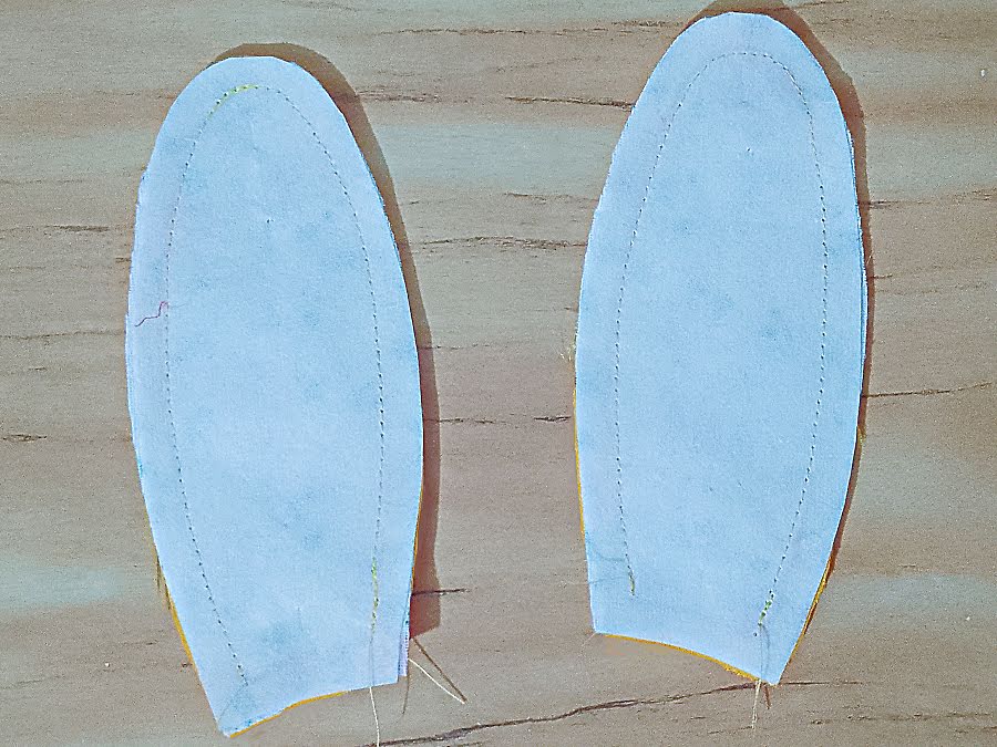 Two ear pieces with fusible interfacing applied to the wrong side, showing the stitched guideline around the ear shape and the open base left unsewn.