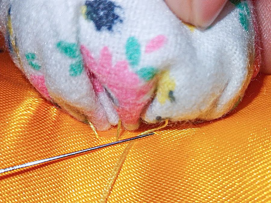 Needle and thread stitching through the gathered edge of the tail and the bunny body, securing the tail with small hand stitches.