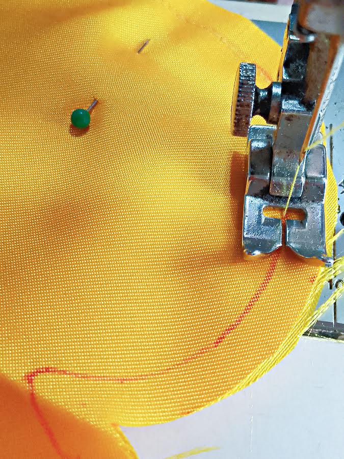 Close-up of a soft toy body being sewn along the traced outline at the sewing machine, showing careful stitching around a curved edge while following the marked seam line.