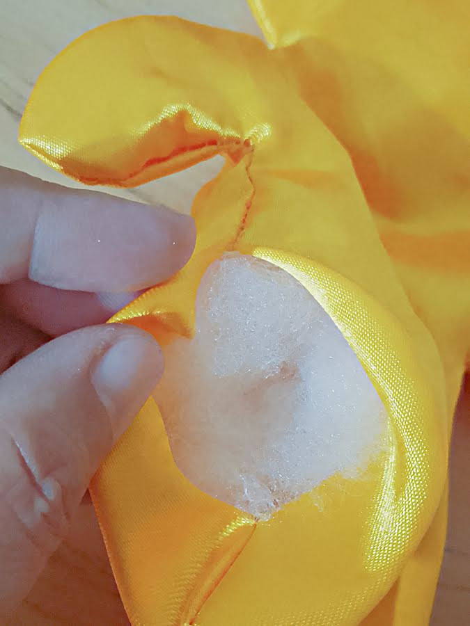 Soft toy body being filled with stuffing through the opening, showing small pieces of fiber added inside to build shape gradually without overfilling.