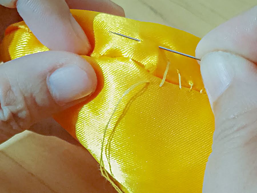 Close-up of the soft toy opening being closed by hand using a ladder stitch, with small, evenly spaced stitches pulled tight to create a nearly invisible seam.
