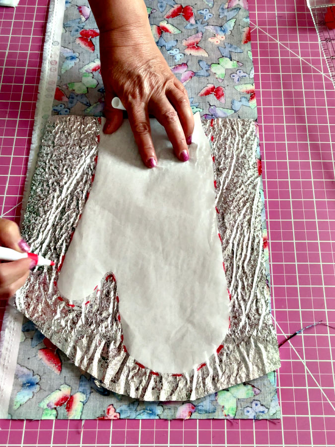 a womans hands holding a marker and the pattern paper arranged on top of the thermal batting preparing for marking