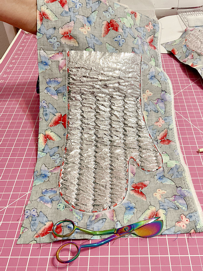 the oven mitt after trimming the batting with the duckbill scissors which are visible in the foreground
