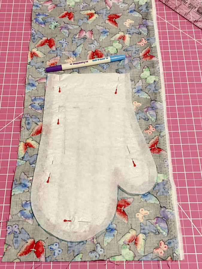 the piece of pattern that includes the seam allowances arranged on top of the oven mitt and pinned in place