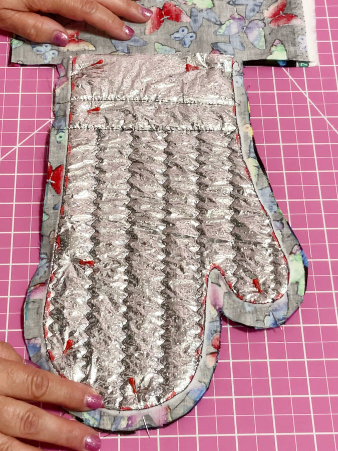 a womans hands holding the two pieces of the mitt placed right side together and pinned in preparation for the final stitch