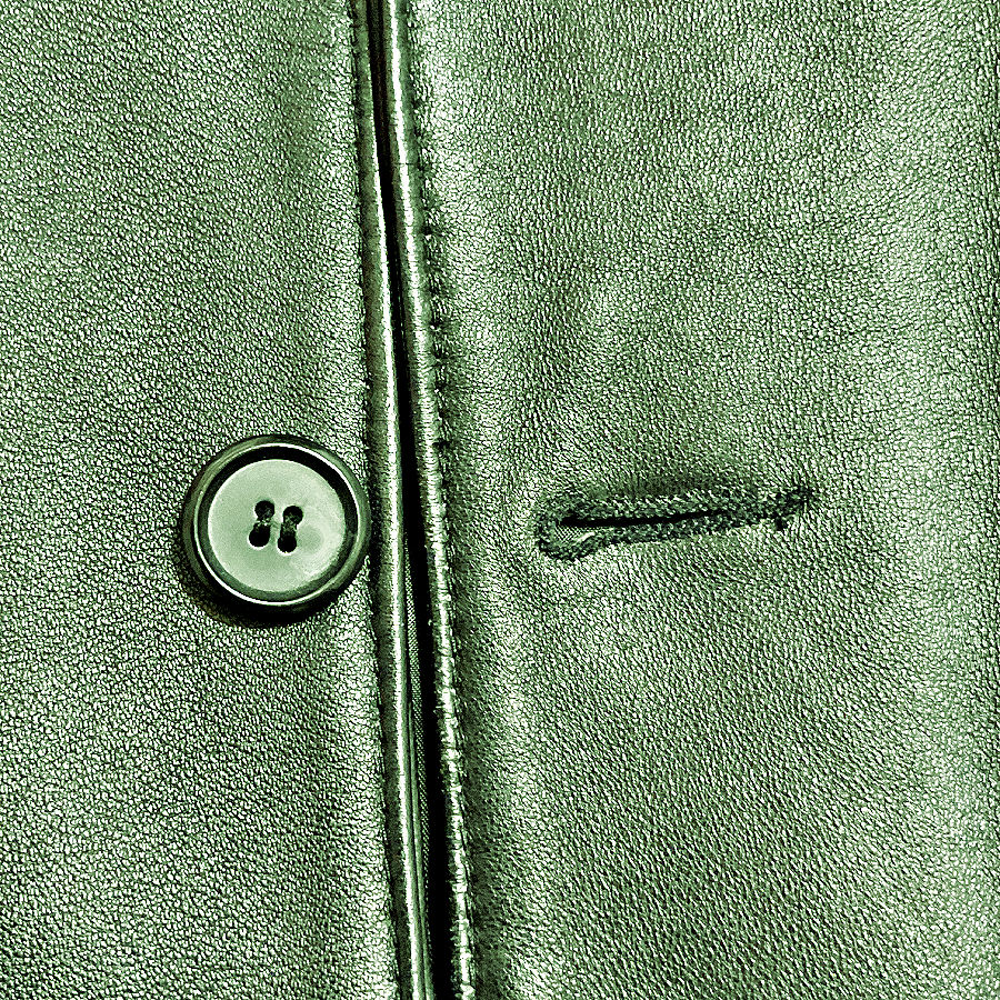 Close-up of a keyhole buttonhole on green leather next to a button and garment edge.