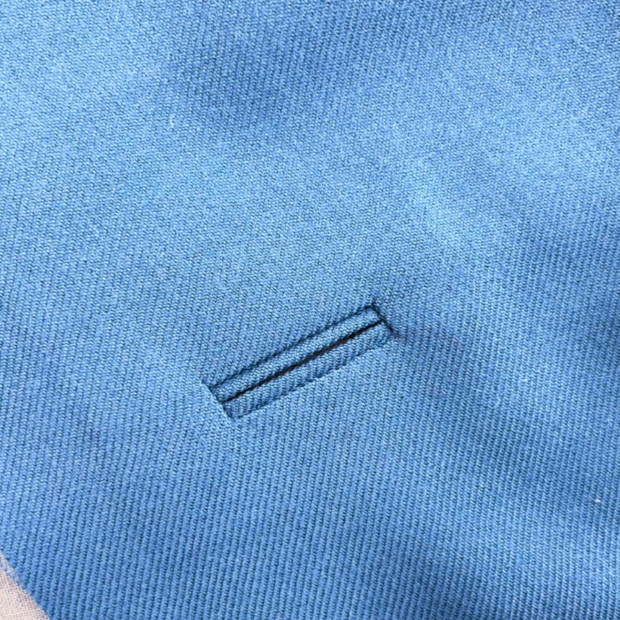 Close-up of a neat bound buttonhole stitched in blue fabric.