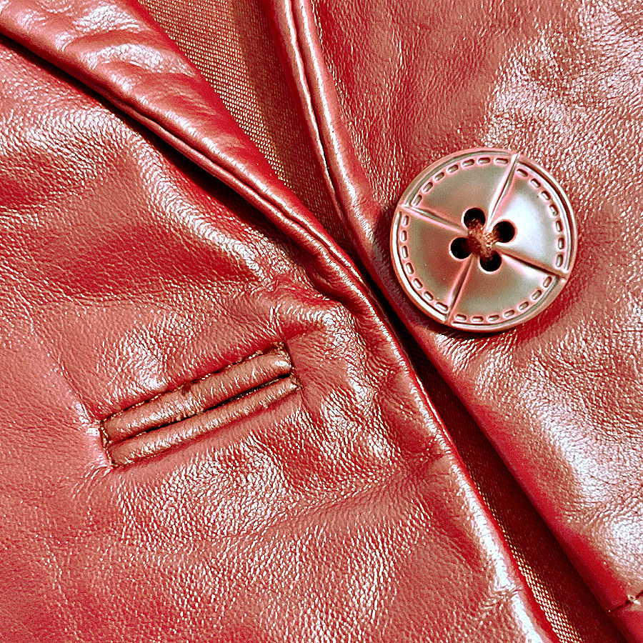 Close-up of a bound buttonhole on shiny red leather beside a large matching button.