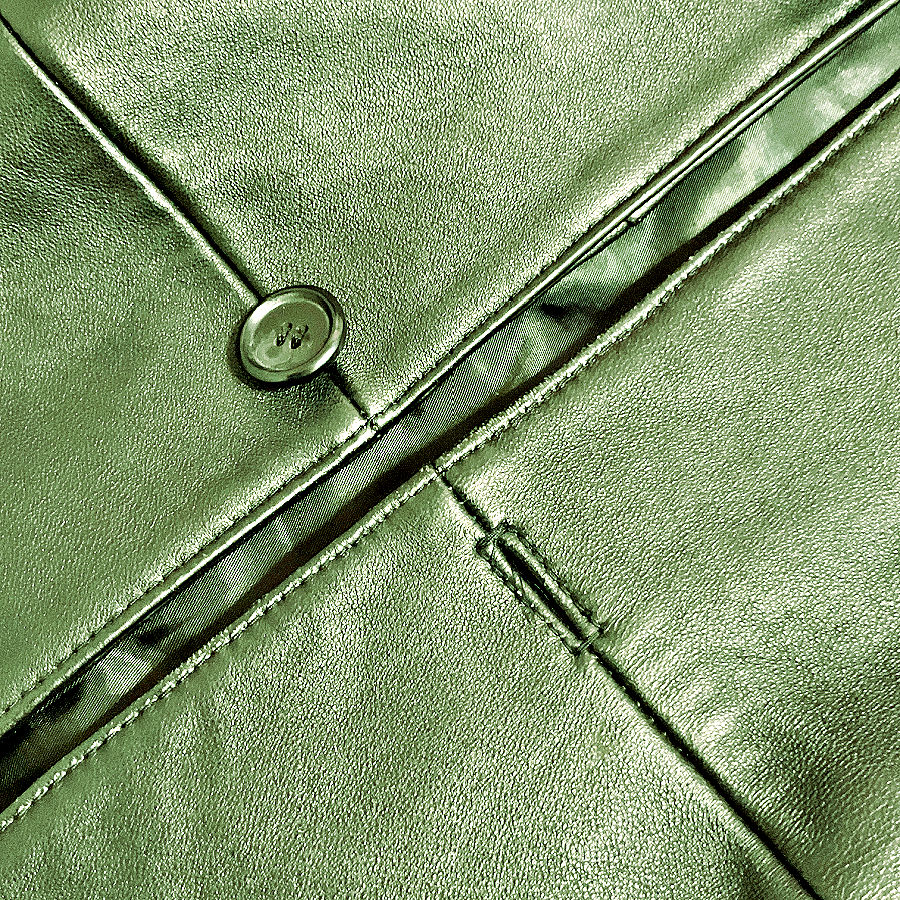 Close-up of a narrow in-seam buttonhole worked into a seam on green leather, with a button nearby.