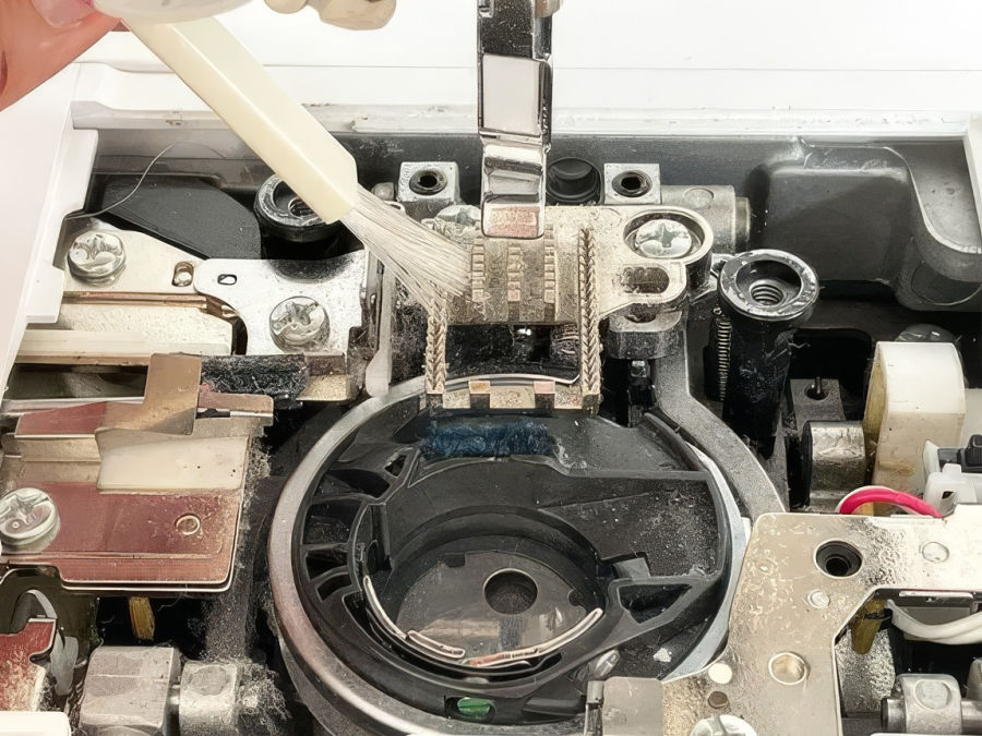a sewing machine bobbin location showing considerable amount of dust and lint while being bruyshed with a small brush