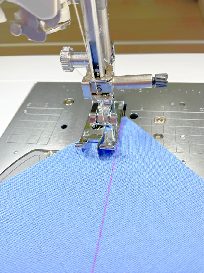 a sewing machine needle assembly with a quarter inch foot being used to sew exactly quarter inch from the diagonal line marked on the fabric