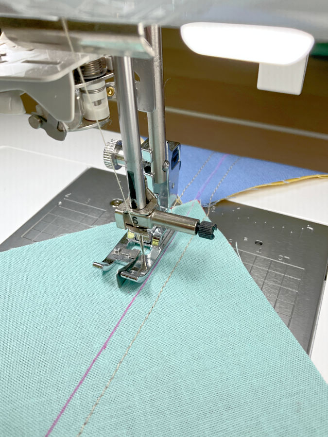 a sewing machine needle assembly with a quarter inch foot being used to sew a second seam from the diagonal line marked on the fabric