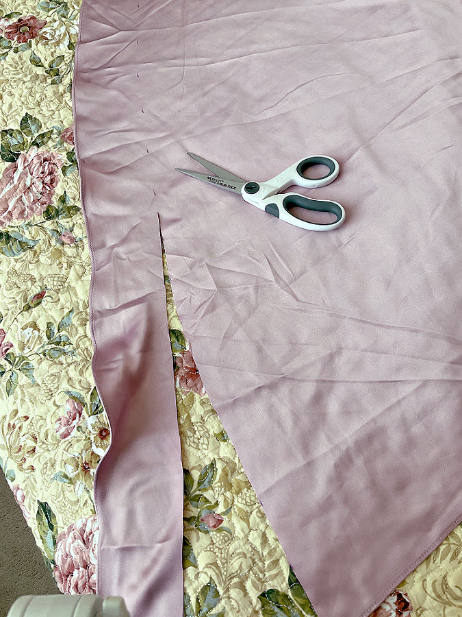the dress that needs to be hemmed shown flat on a bed while a strip is cut from the hem a pair of scissors sits on the bed also