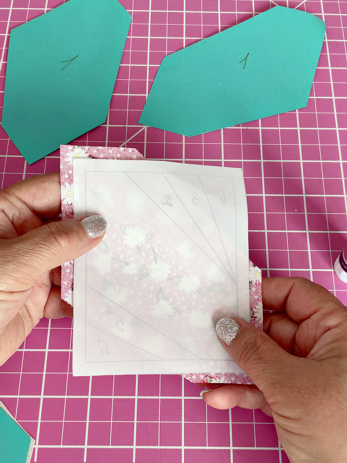 a womans hands holding the vellum template with the attached piece of fabric on the other side checking the alignment of the piece