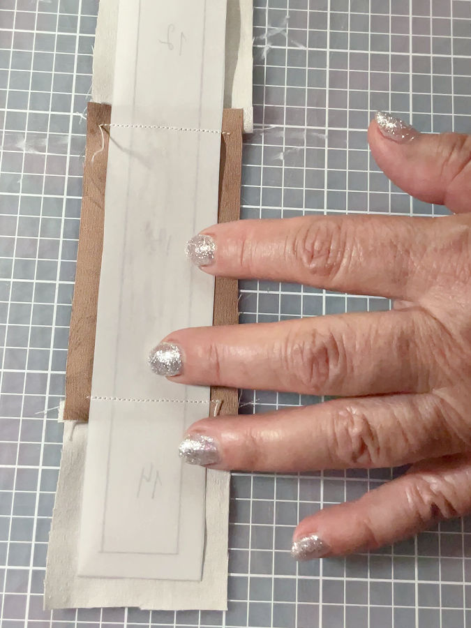 a womans hand showing the butterfly body after stitching the paper still attached