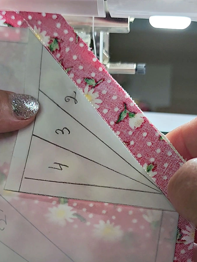 a womans hand holding the piece the seam visible near the paper edge the beginning of the seam beyond the paper