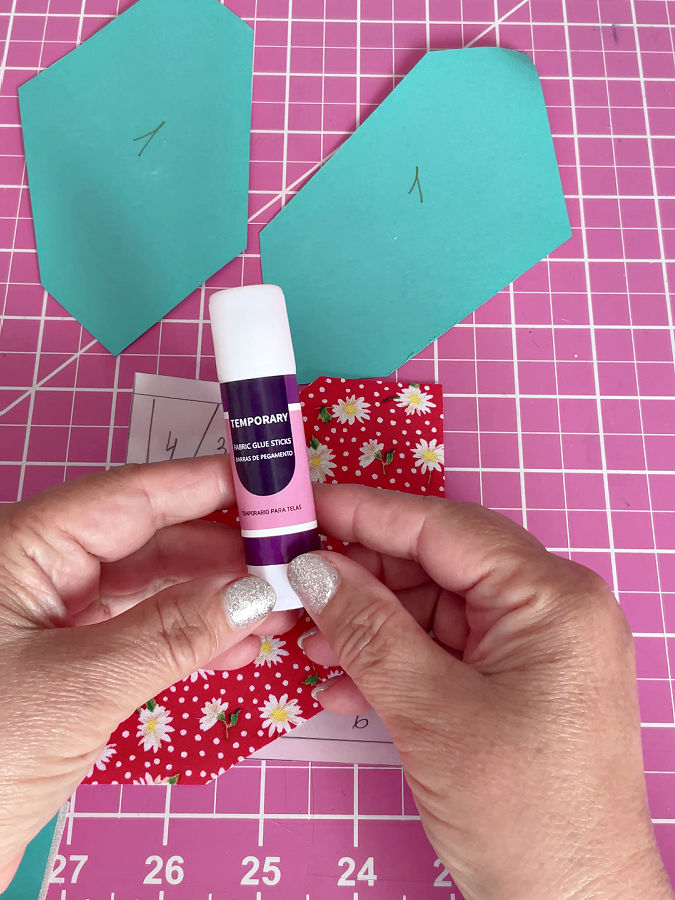 a womans hands holding a stick of glue to attach the fabric to the template temporarily