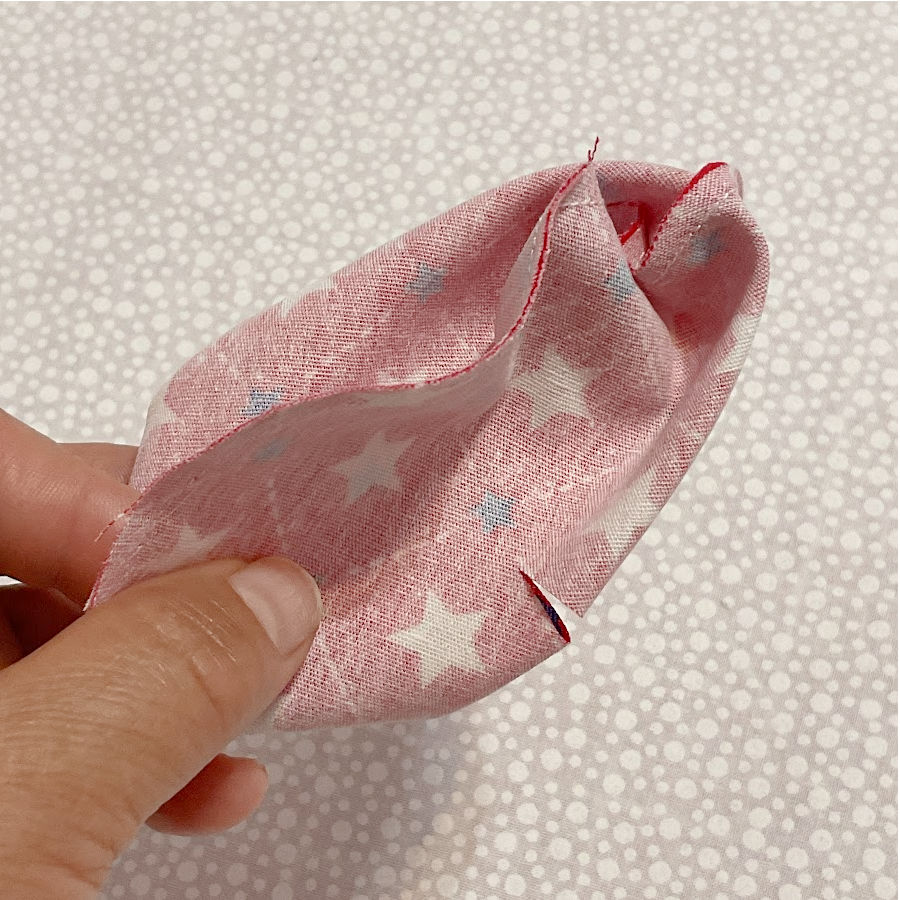 a womans hand pinching the fabric circles sewn together showing a small cut in the center of one side