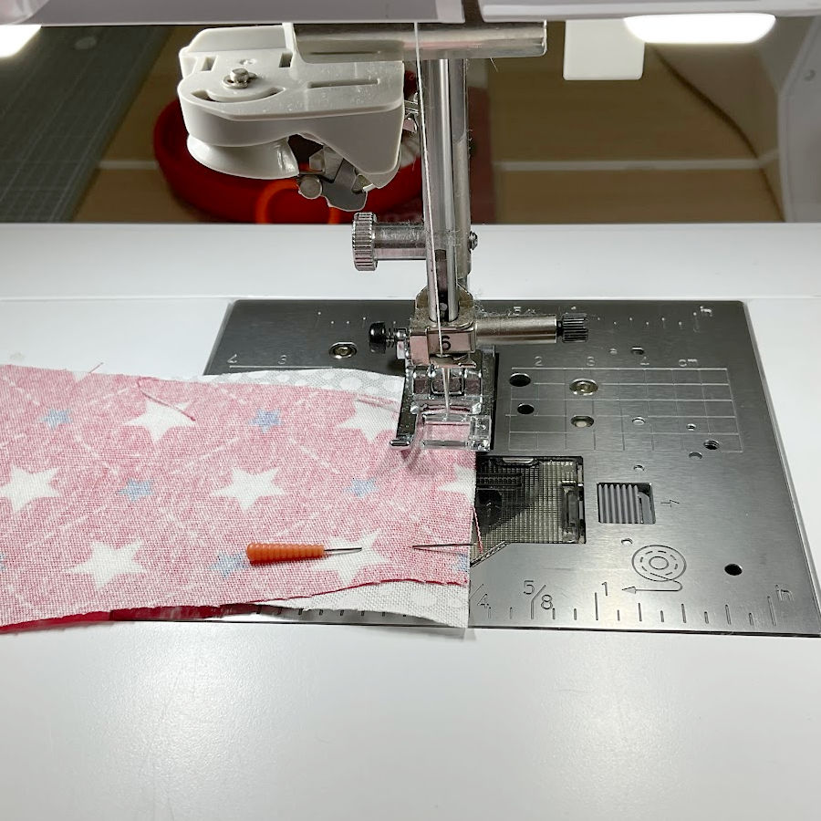 a sewing machine needle assembly shown while sewing the red and white pieces together
