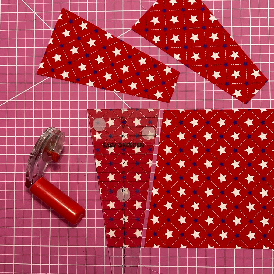 Trapezoidal ruler placed on a piece of material with some pieces already cut shown a rotary cutter also in the image