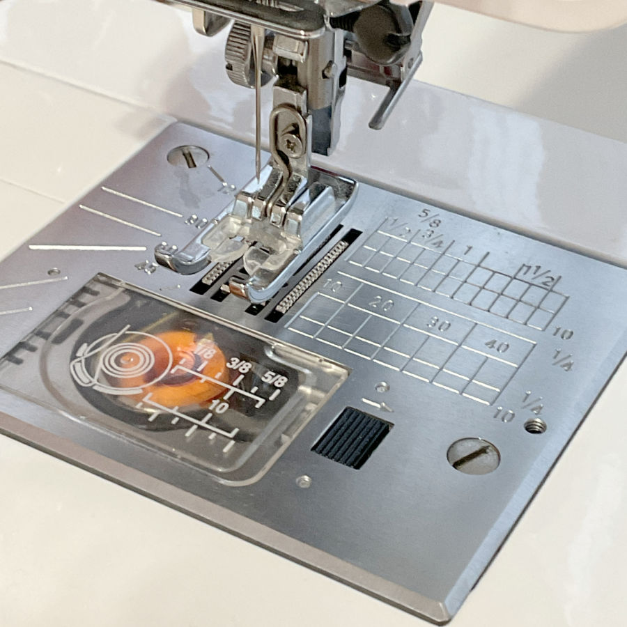 a close up image of the throat plate of a sewing machine with various helpful markings on it both in centimeters and inches