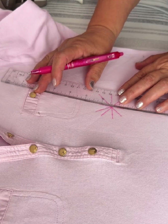 a womans hands holding a ruler and a pen while drawing lines over the stained area on a blouse