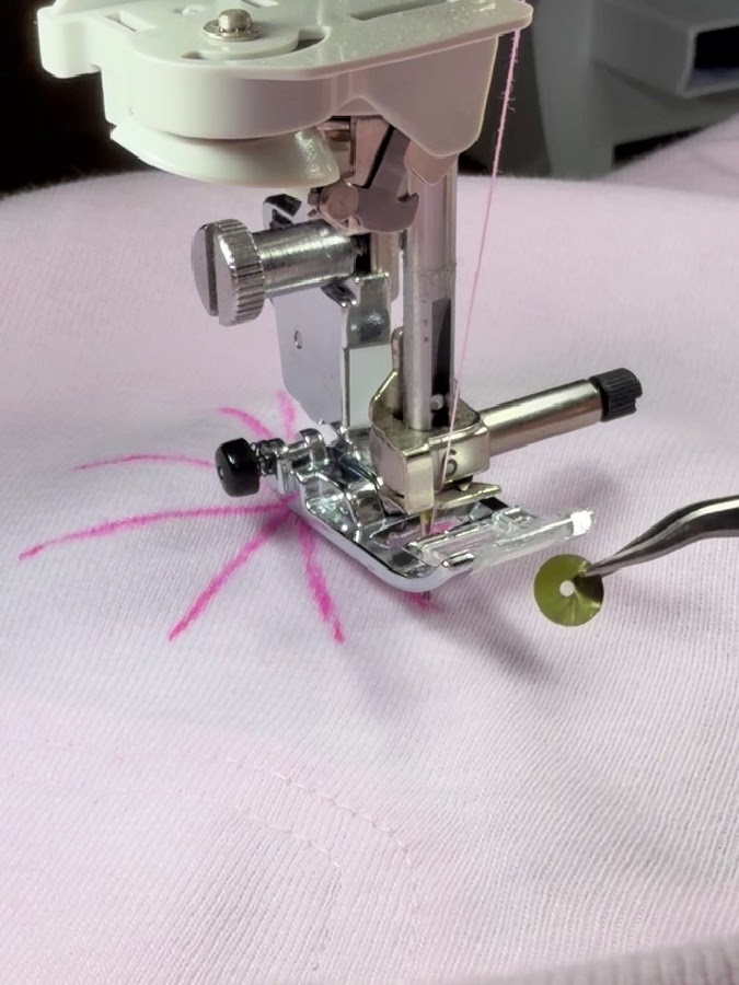 a sewing machine needle assembly ready to sew a sequin held by tweezers in front of the needle