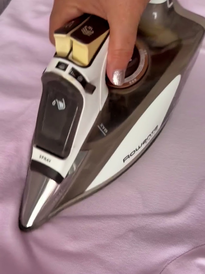 a womans hand using a hot iron to iron the pink blouse