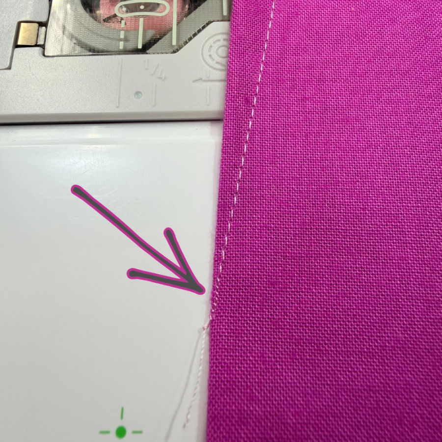 a piece of material on a sewing machine table an arrow points at the end of the dart where the stitches have a smaller length