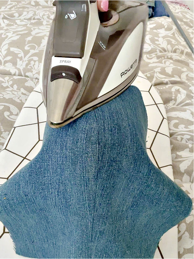 a rowenta hot iron while pressing a piece of denim on the right side on the corset ironing board
