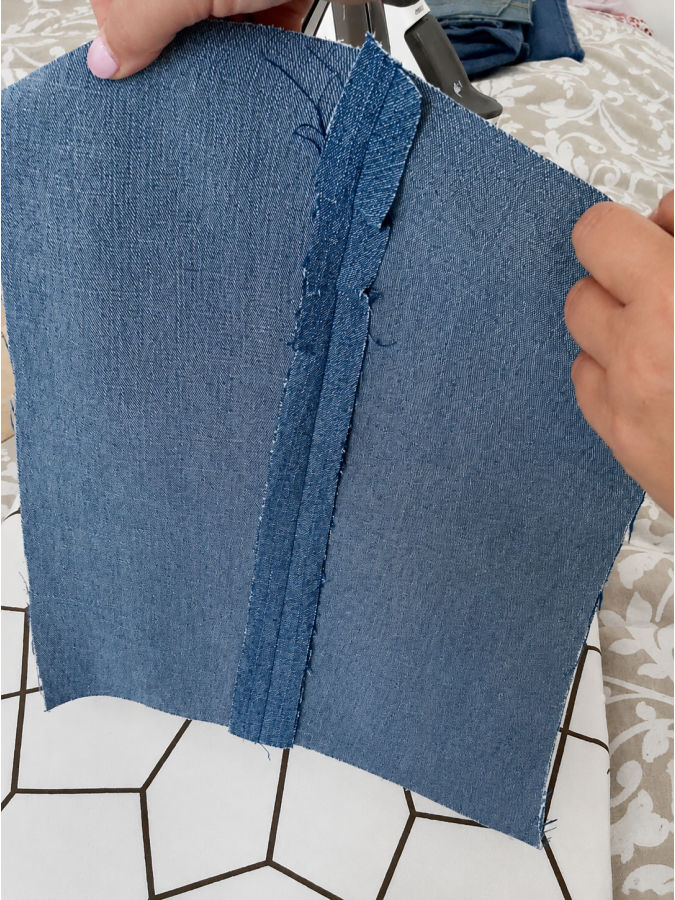a womans hands holding a piece of denim with a seam after pressing