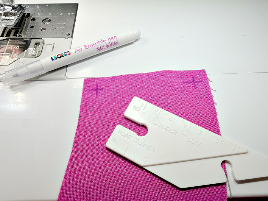 a point turner ruler sitting on a piece of material with two turning points marked with an air erasable pen also visible in the image