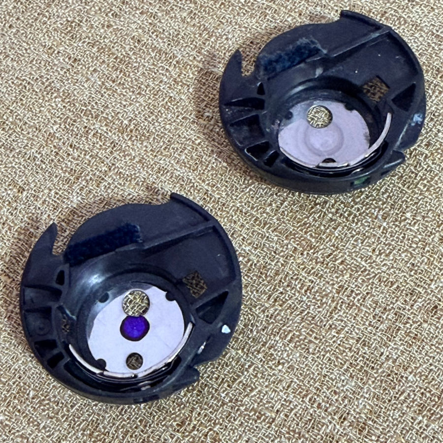 two bobbin cases apparently identical laying on a piece of fabrfic