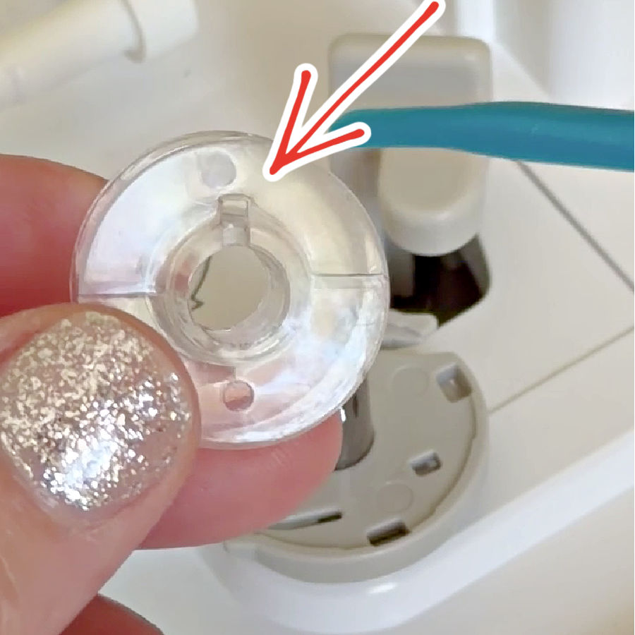 a womans hand holding a plastic bobbin an arrow pointing to a notch in the plastic