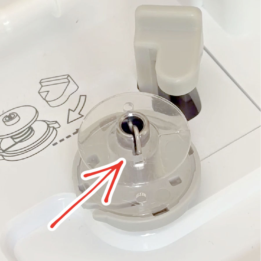 a bobbin installed in the bobbin winding mechanism of a sewing machine an arrow pointing to a small spring that is designed to keep the bobbin in place while winding