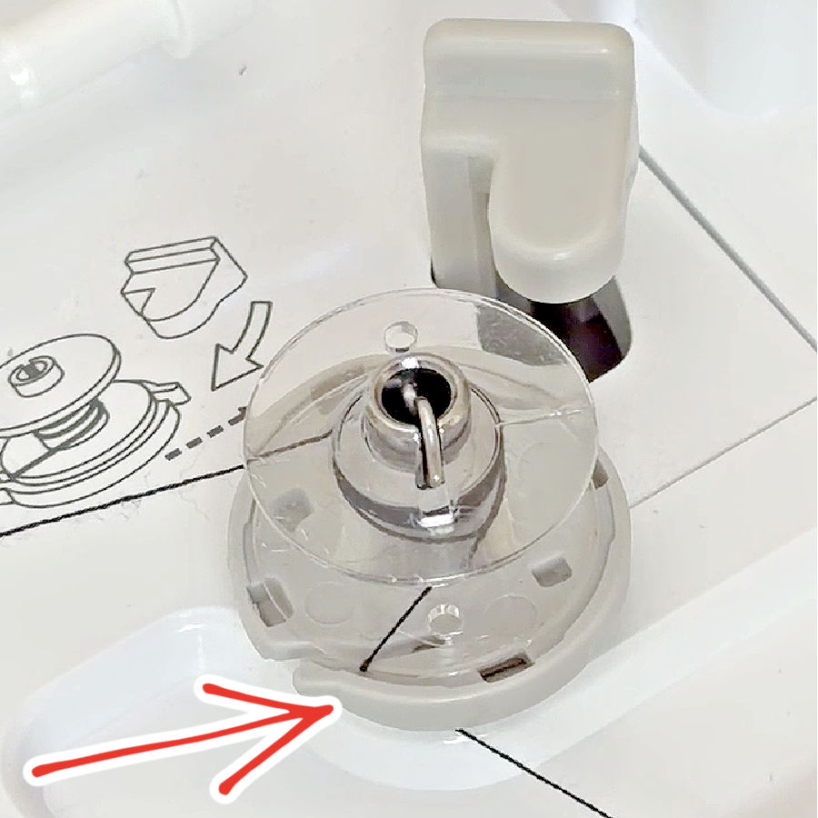 a bobbin installed in a sewing machine bobbin winding mechanism an arrow points to the thread cutter which is part of the bobbin winder
