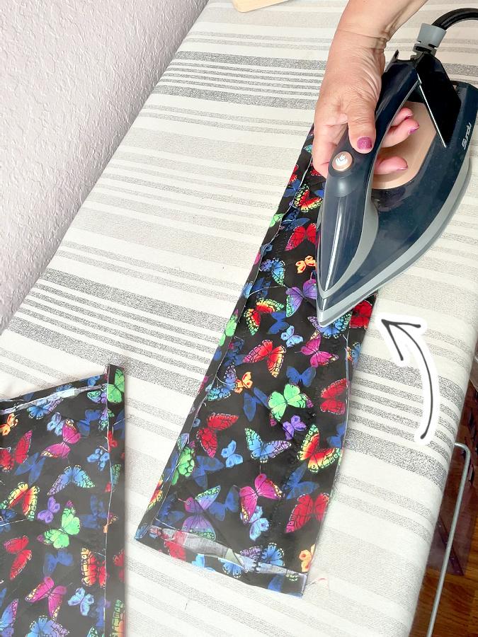 a womans hand holds a hot iron while ironing the folds made previously an arrow points to the fold