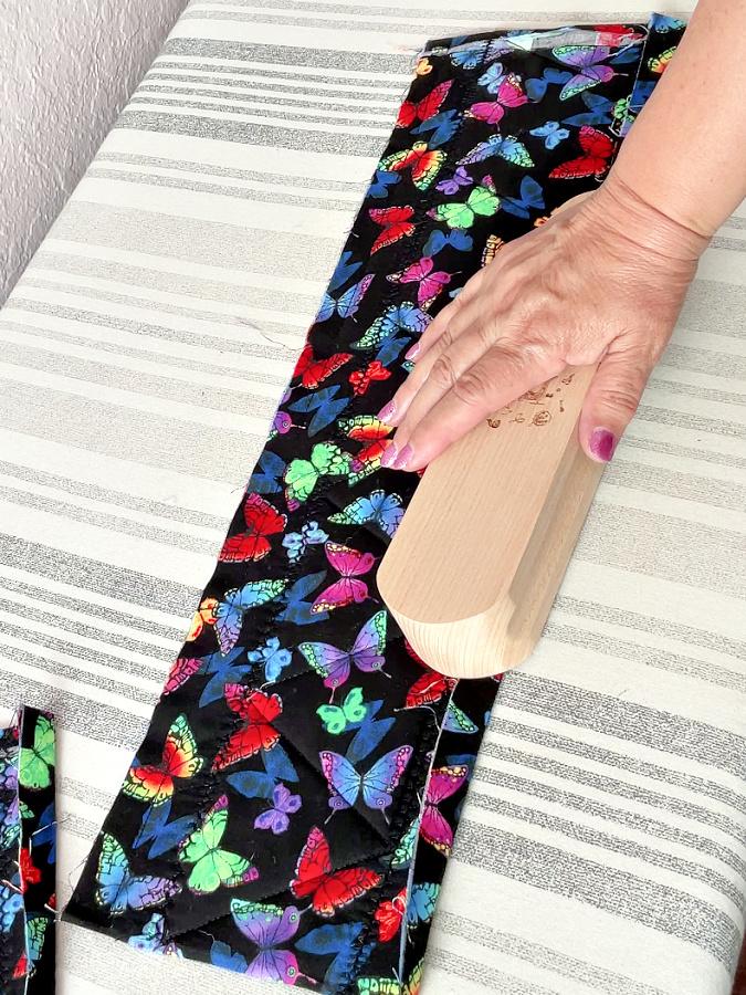a womans hand shown while pressing the fabric with the tailors clapper