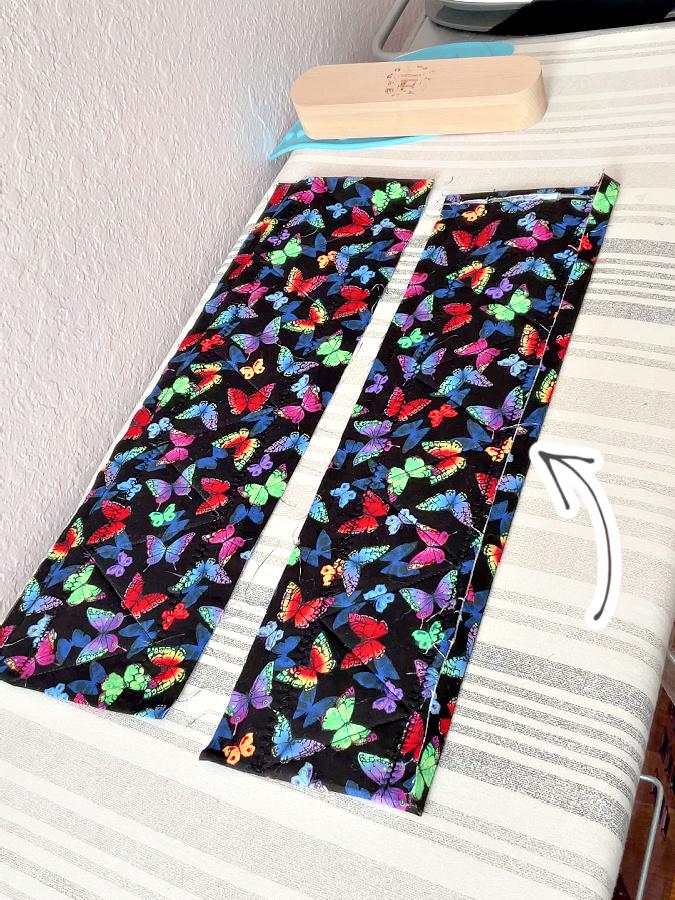 two pieces of material lay down on an ironing board an arrow points to the fold line drawn previously