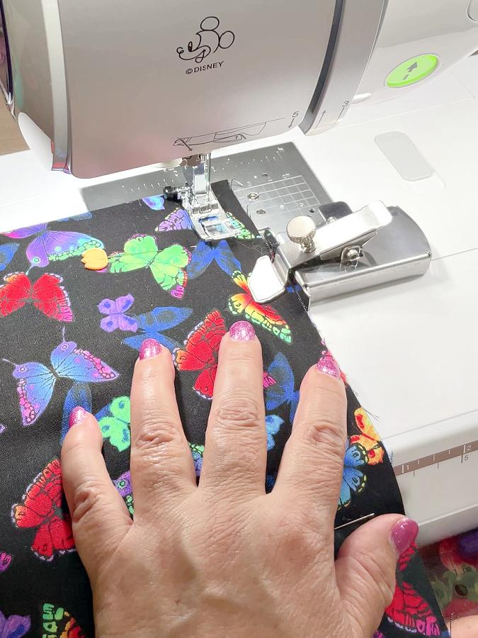 a womans hand guides a piece of fabric for a sewing machine