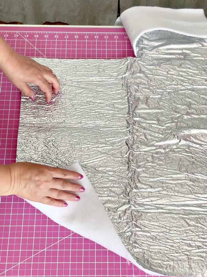 a womans hands shyows a piece of insulating batting a corner of the batting is folded to show both sides one is shiny the other is not