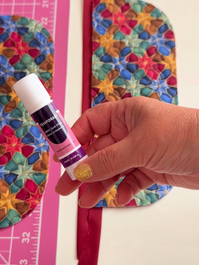 a womans hand holds a fabric glue stick pieces of the armrest organizer in the background
