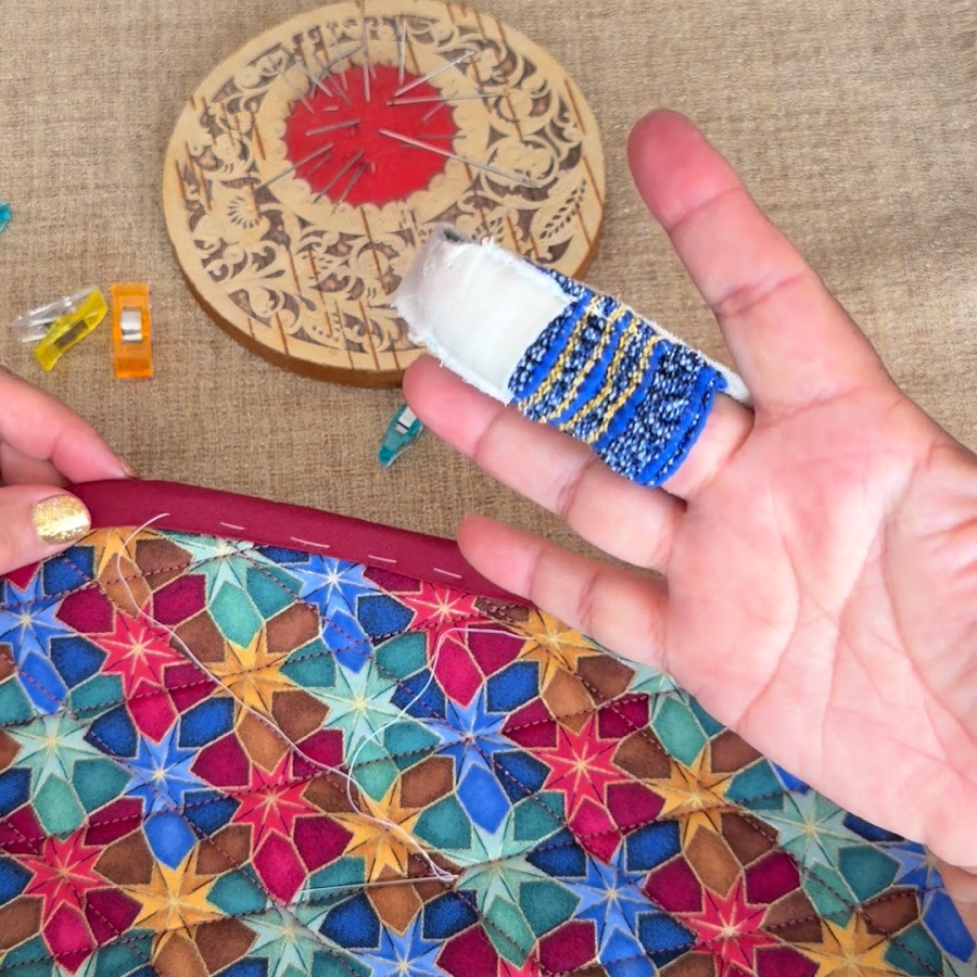 a womans hand with a thimble attached on the middle finger the organizer assembly in the background