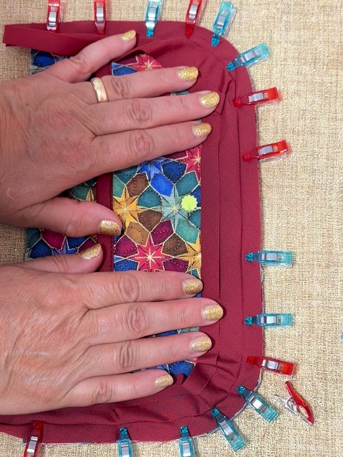 using clips to attach the binding to the curved side of the organizer assembly a womans hands pressing on the fabric clips holding the edges