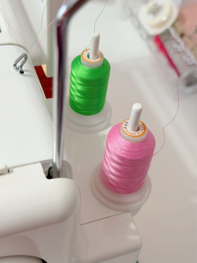 two spools of thread one green one pink installed in the main and auxiliary spool pins on a sewing machine
