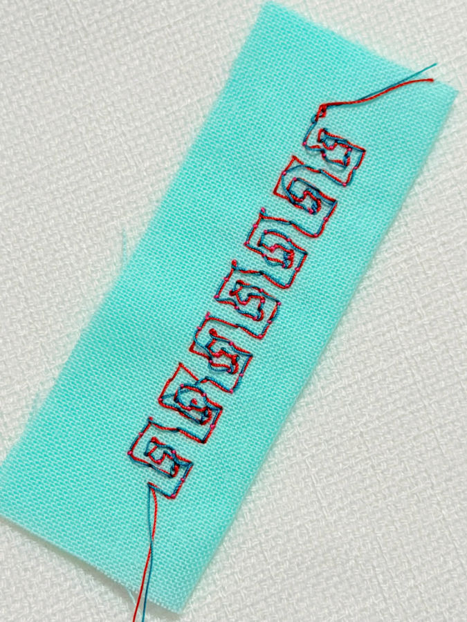 a square decorative stitch made using a double eye needle and red and green thread
