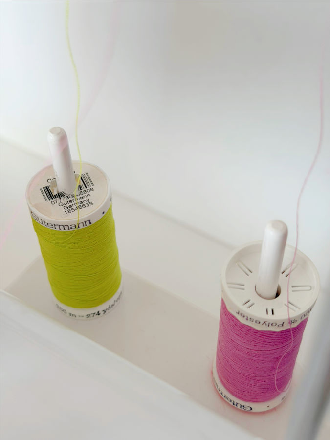 two Gütermann polyester thread spools of differtent colors installed in on the spool pins in a sewing machine