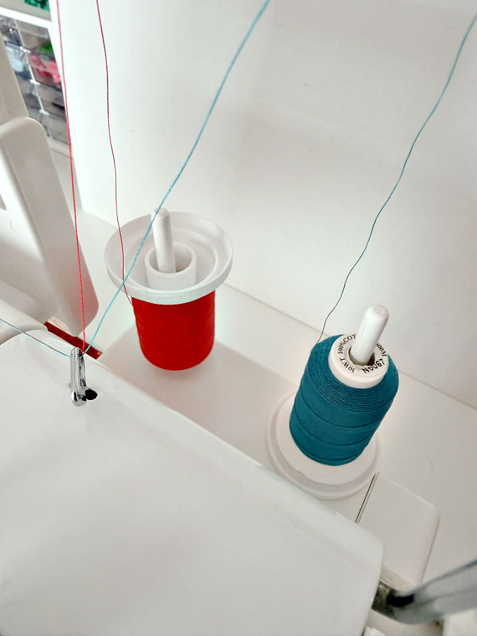 two cotton embroidery thread spools installed on the spool pins in a sewing machine