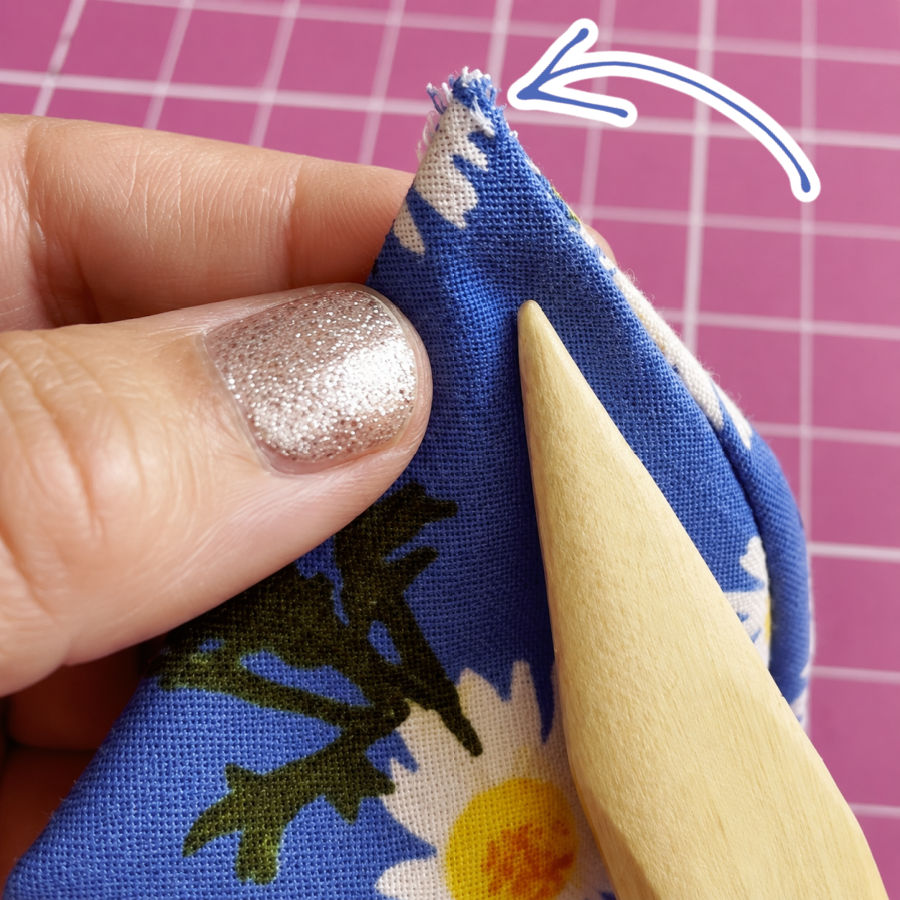 a womans hand holds a piece of material an arrow points to a corner of the material where the stitching came apart